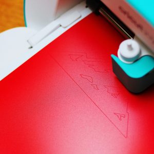 Close-up of a cutting machine engraving a pattern on red paper indoors.